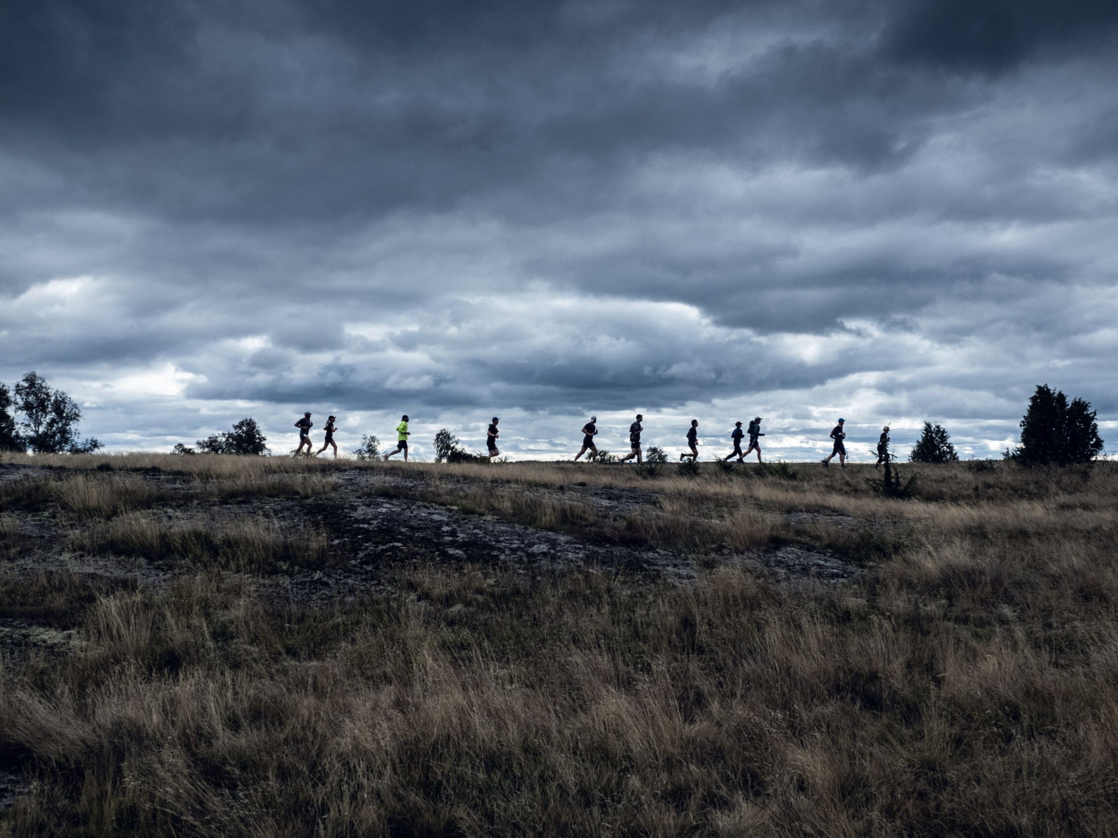Runners silhouetted on the flat heathland ridge of Sörmland, Sweden, with dramatic storm clouds overhead
